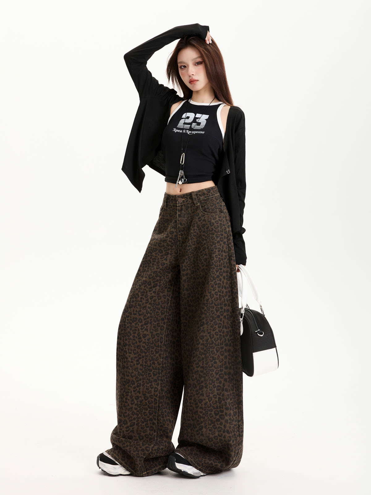 YEEYEEWang Wide-Leg Jeans in Leopard Print, Asian-fit cut, full-body standing pose with one arm raised overhead, black cardigan draped off the shoulders, holding a black-and-white handbag.