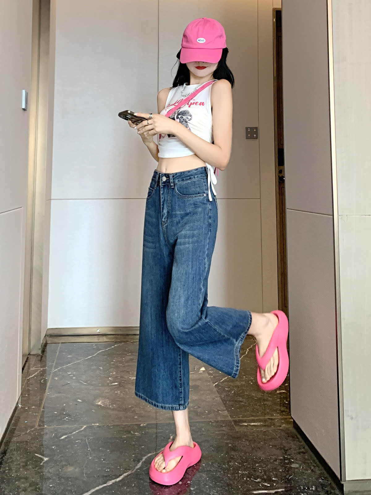 YEEYEEWang Wide-Leg Jeans in Vintage Blue, Asian-fit cut, full-body leg-kick pose checking phone, showing the Cropped (8) hem, pink cap and sandals.