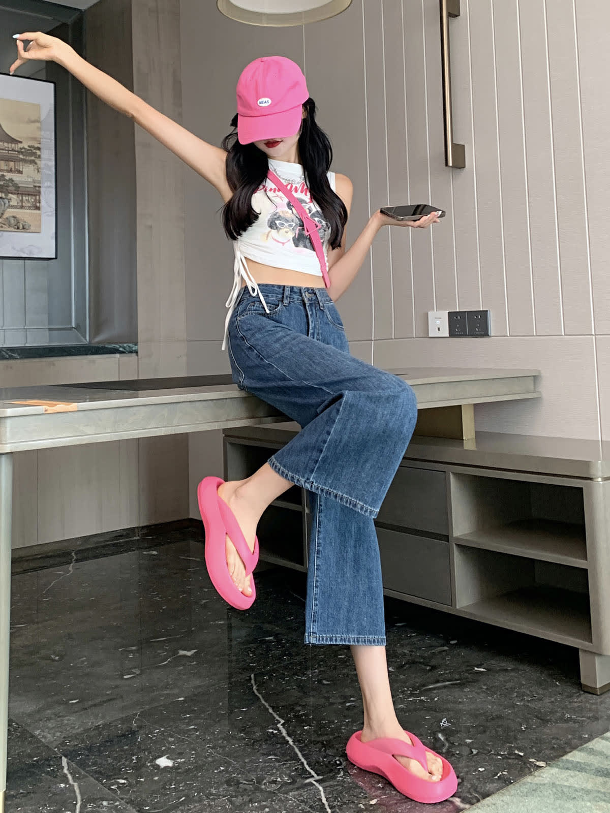 YEEYEEWang Wide-Leg Jeans in Vintage Blue, Asian-fit cut, full-body side seated pose on table edge with one arm raised and leg lifted, holding phone, pink cap.
