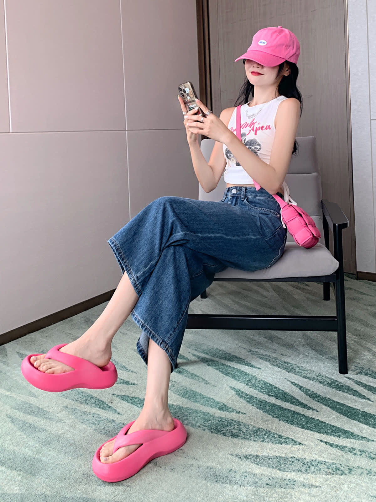 YEEYEEWang Wide-Leg Jeans in Vintage Blue, Asian-fit cut, seated side view on chair holding phone with both hands, pink cap and platform sandals.