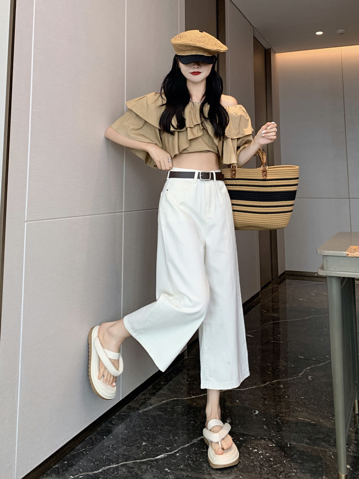 YEEYEEWang Wide-Leg Jeans in Ivory, Asian-fit cut, full-body side pose leaning against wall with one foot raised on the wall, striped straw tote on arm, woven cap.