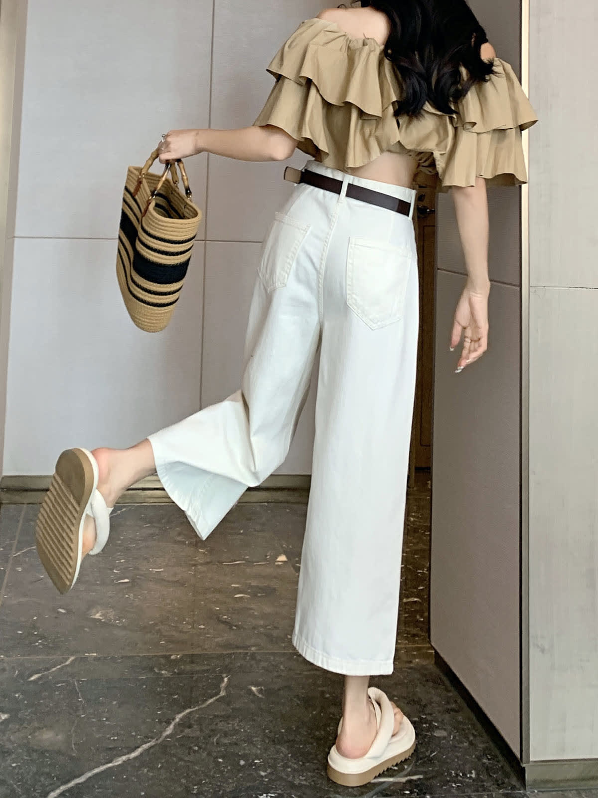 YEEYEEWang Wide-Leg Jeans in Ivory, Asian-fit cut, full-body back view with one leg kicked back, carrying striped straw tote, brown belt at waist.