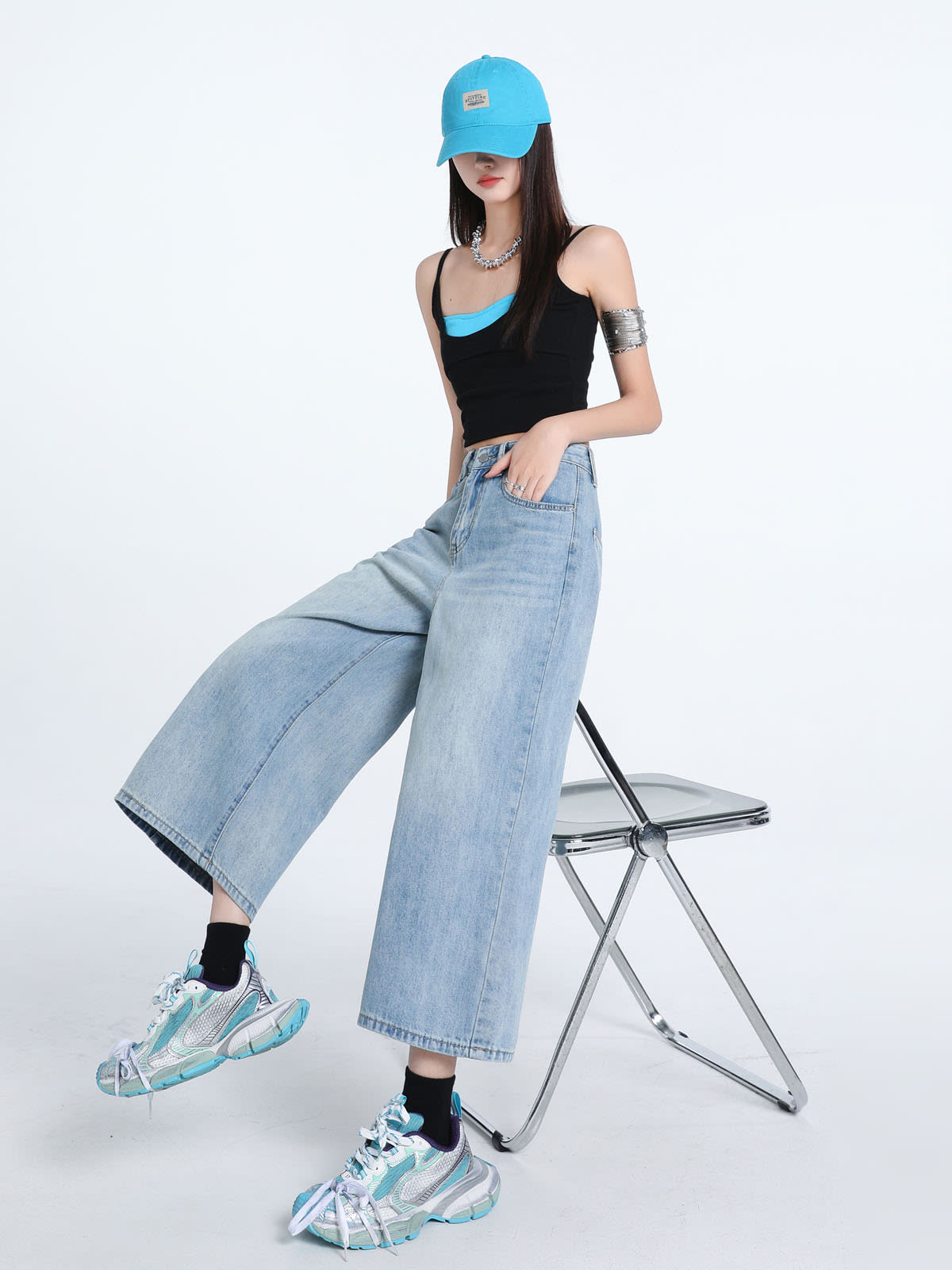 YEEYEEWang Wide-Leg Jeans in Light Blue, Asian-fit cut, full-body seated pose on a clear folding chair with one leg extended, hand in front pocket, blue cap.