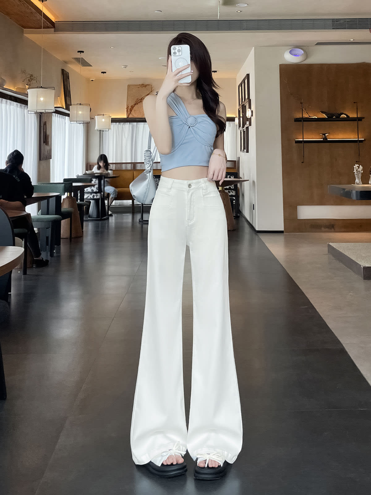YEEYEEWang Flare Jeans in White, Asian-fit cut, full-body front pose holding phone at face, silver shoulder bag and stacked fluid hems.
