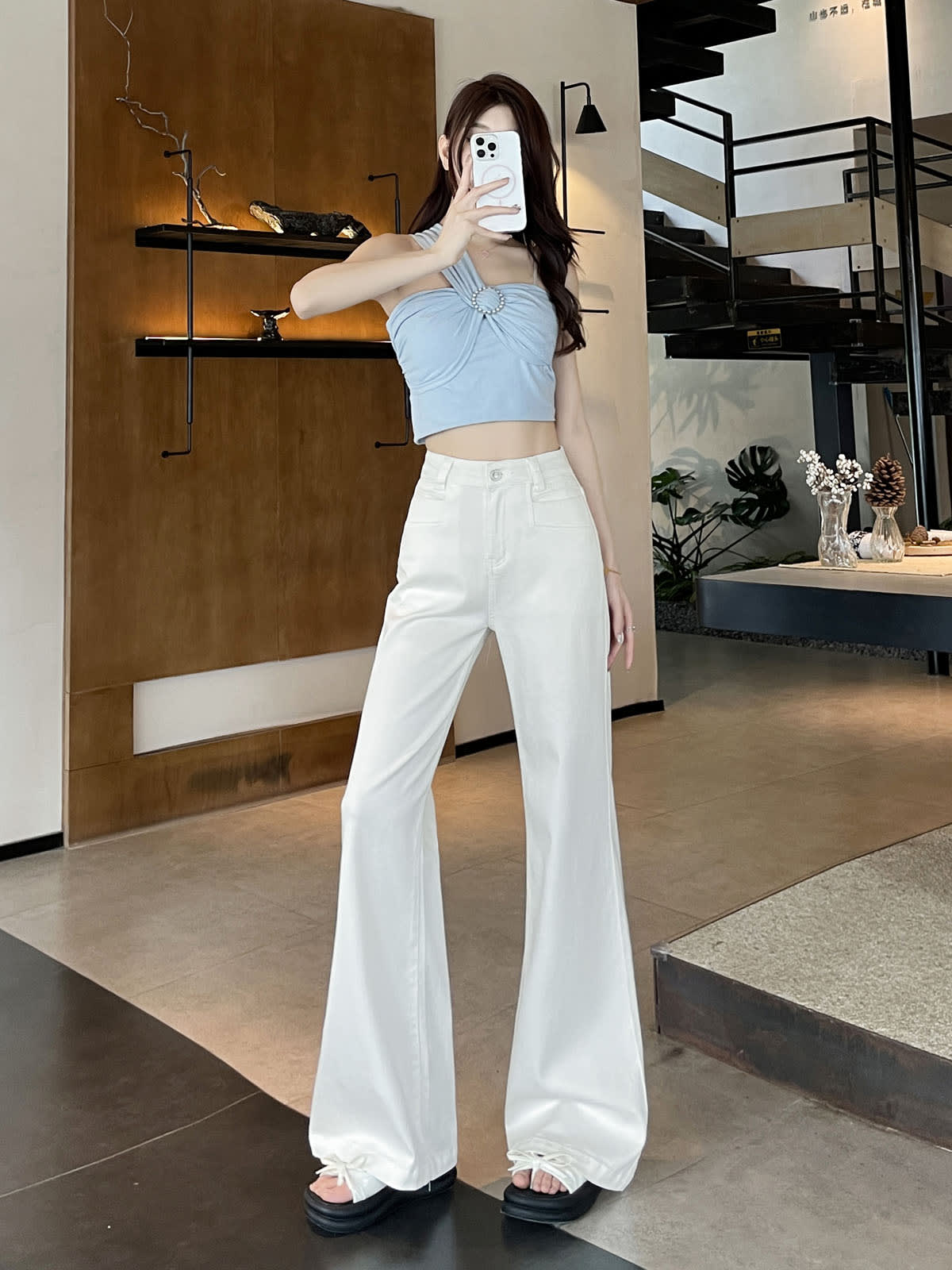 YEEYEEWang Flare Jeans in White, Asian-fit cut, full-body three-quarter pose holding phone at face, light blue halter top and stacked fluid hems.