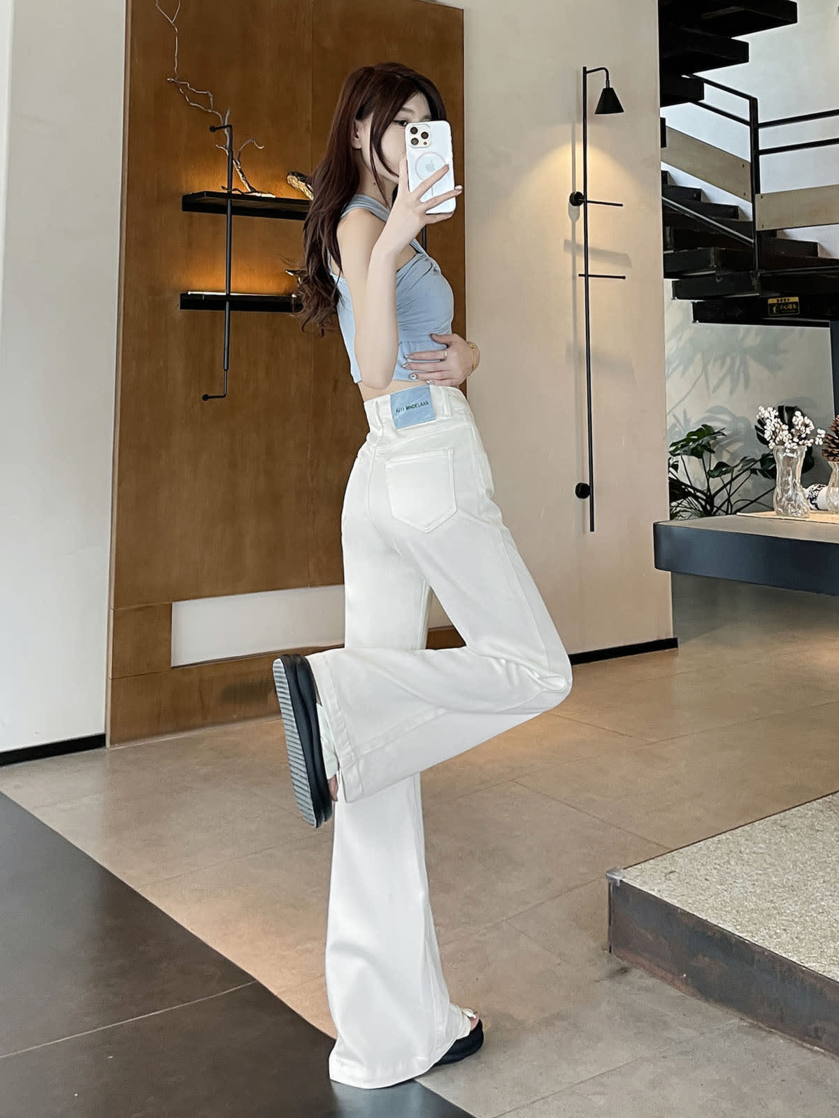 YEEYEEWang Flare Jeans in White, Asian-fit cut, full-body side leg-kick pose holding phone at face, showing side seam and back pocket.