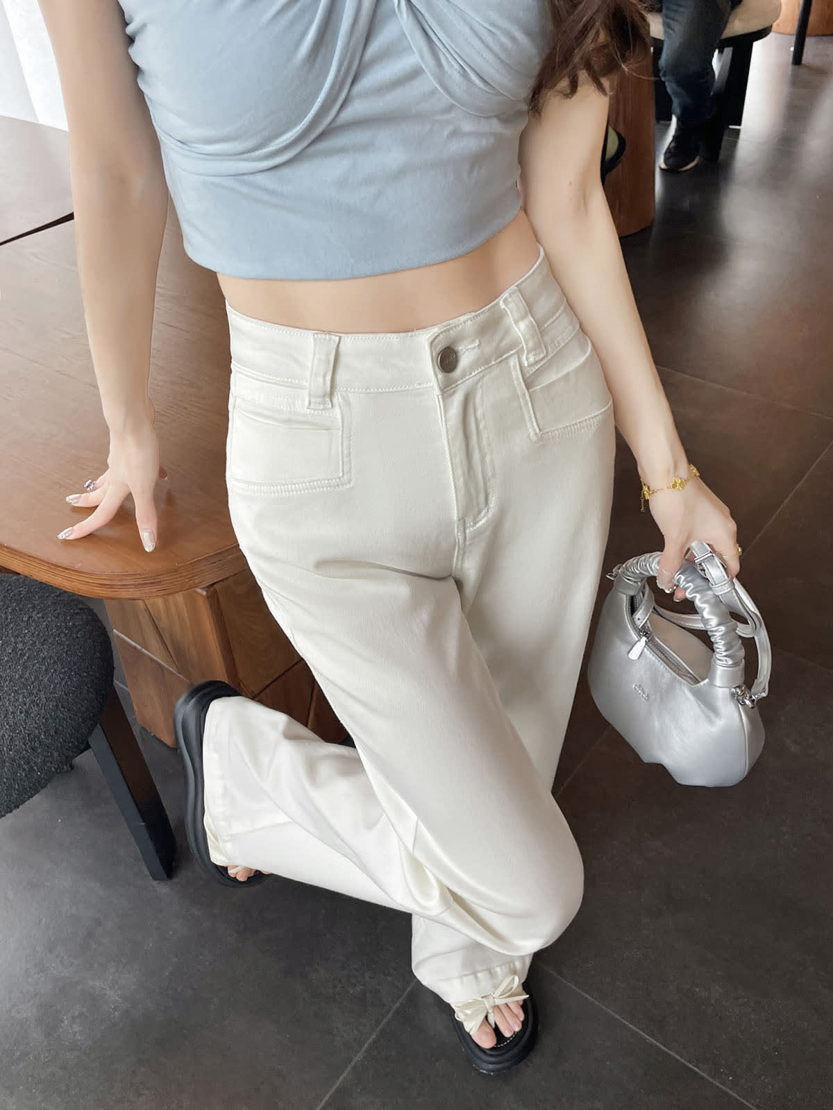 YEEYEEWang Flare Jeans in White, Asian-fit cut, waist-down front view standing by wooden table, holding silver handbag.