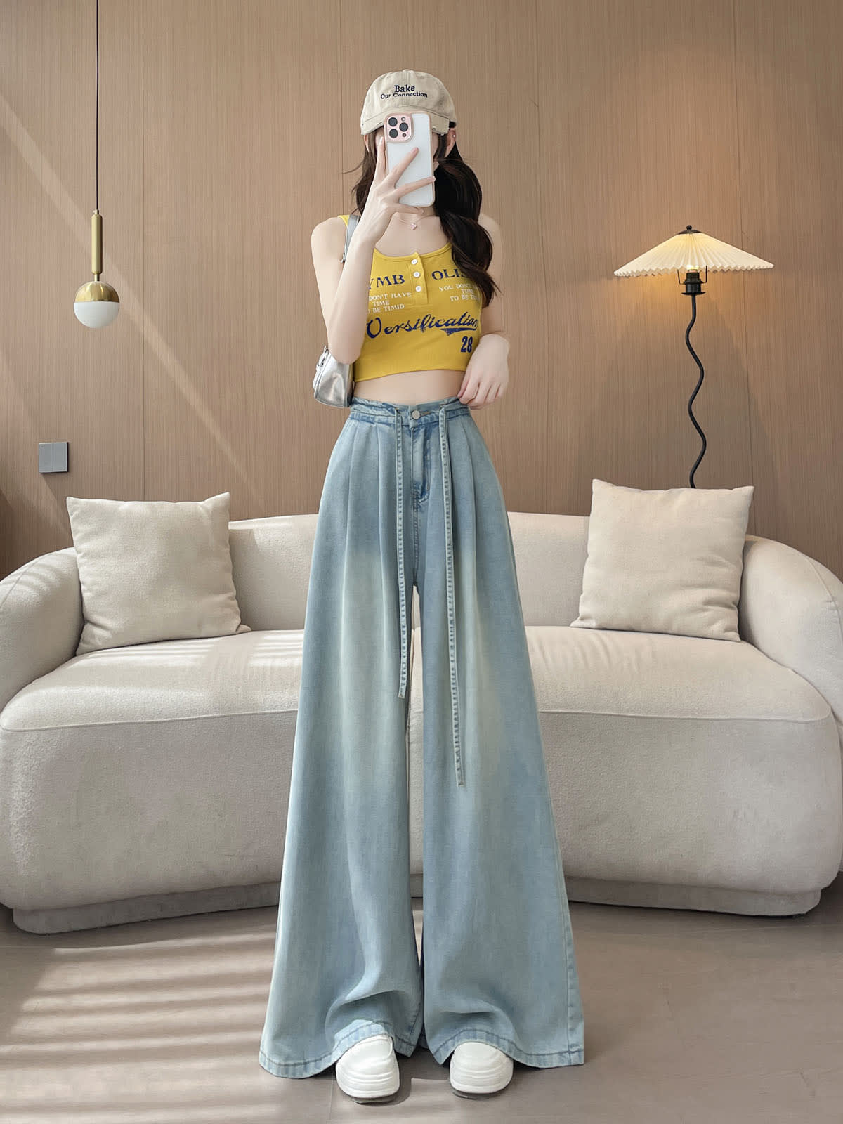 YEEYEEWang Wide-Leg Jeans in Light Blue, Asian-fit cut, full-body front standing pose holding phone at face, yellow tank and beige cap with silver shoulder bag.