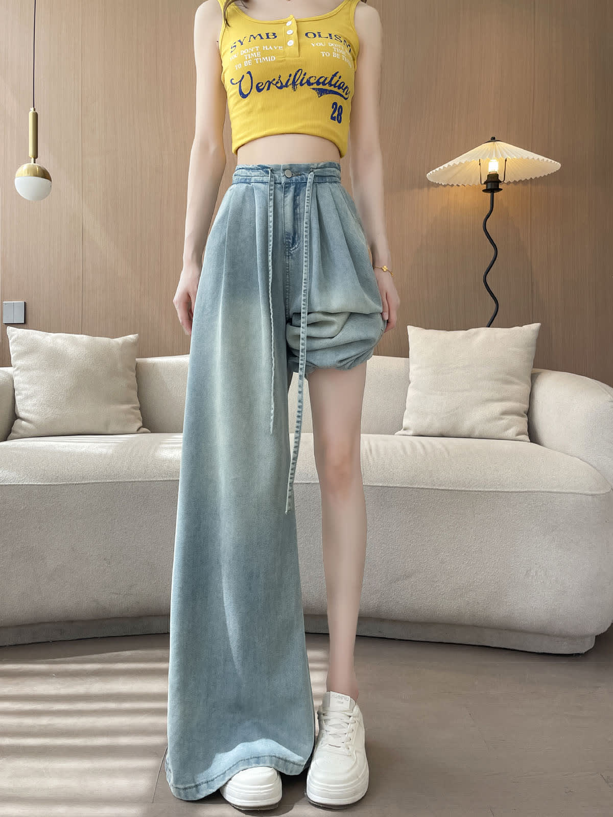 YEEYEEWang Wide-Leg Jeans in Light Blue, Asian-fit cut, full-body standing pose with one pant leg pulled up to the thigh showing the wide leg opening, white sneakers visible.