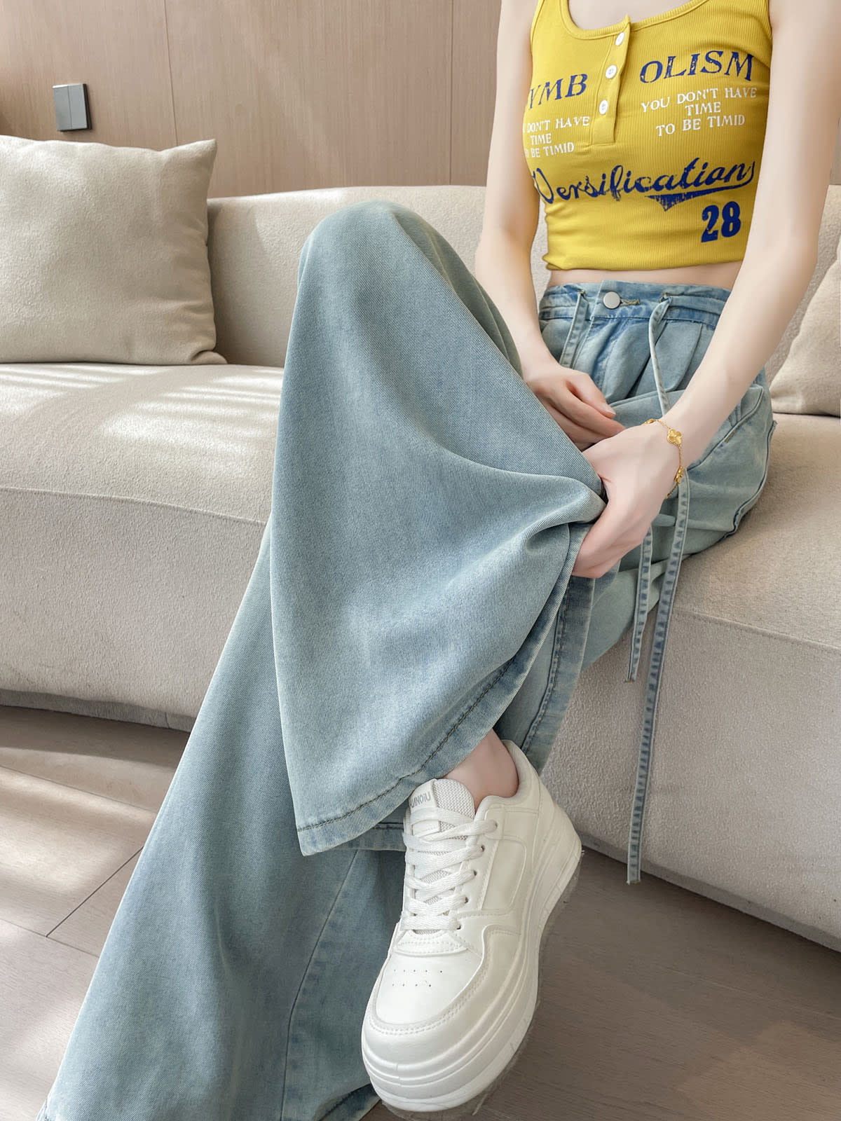 YEEYEEWang Wide-Leg Jeans in Light Blue, Asian-fit cut, waist-down seated pose on sofa with crossed leg, soft denim drape close view.