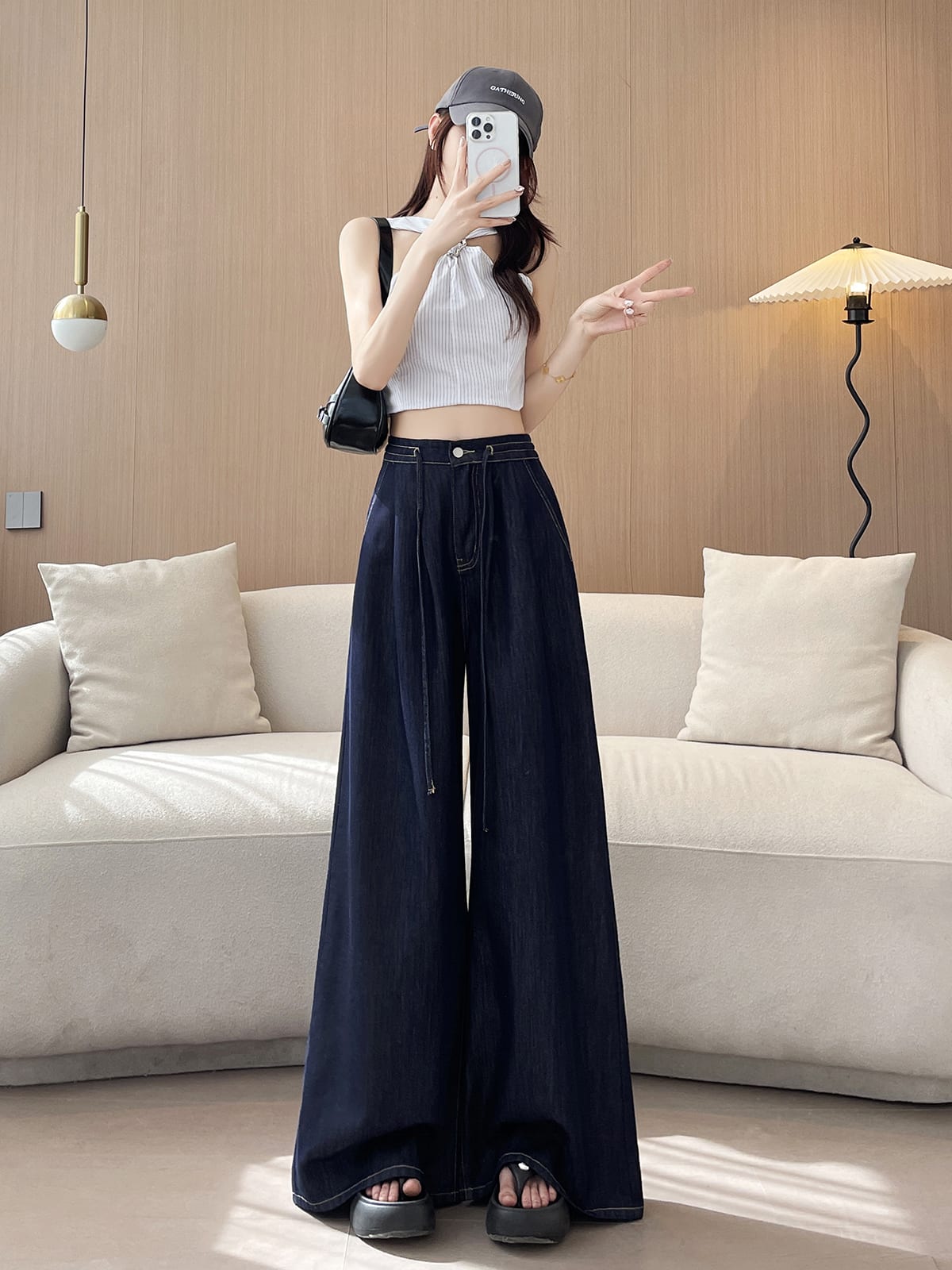 YEEYEEWang wide-leg jeans in Denim Blue, Asian-fit cut, full-body front pose holding phone at face, cap and striped halter top, black bag on shoulder.