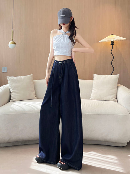 YEEYEEWang wide-leg jeans in Denim Blue, Asian-fit cut, full-body standing pose with hand resting on waistband, striped halter top and gray cap, indoor sofa scene.