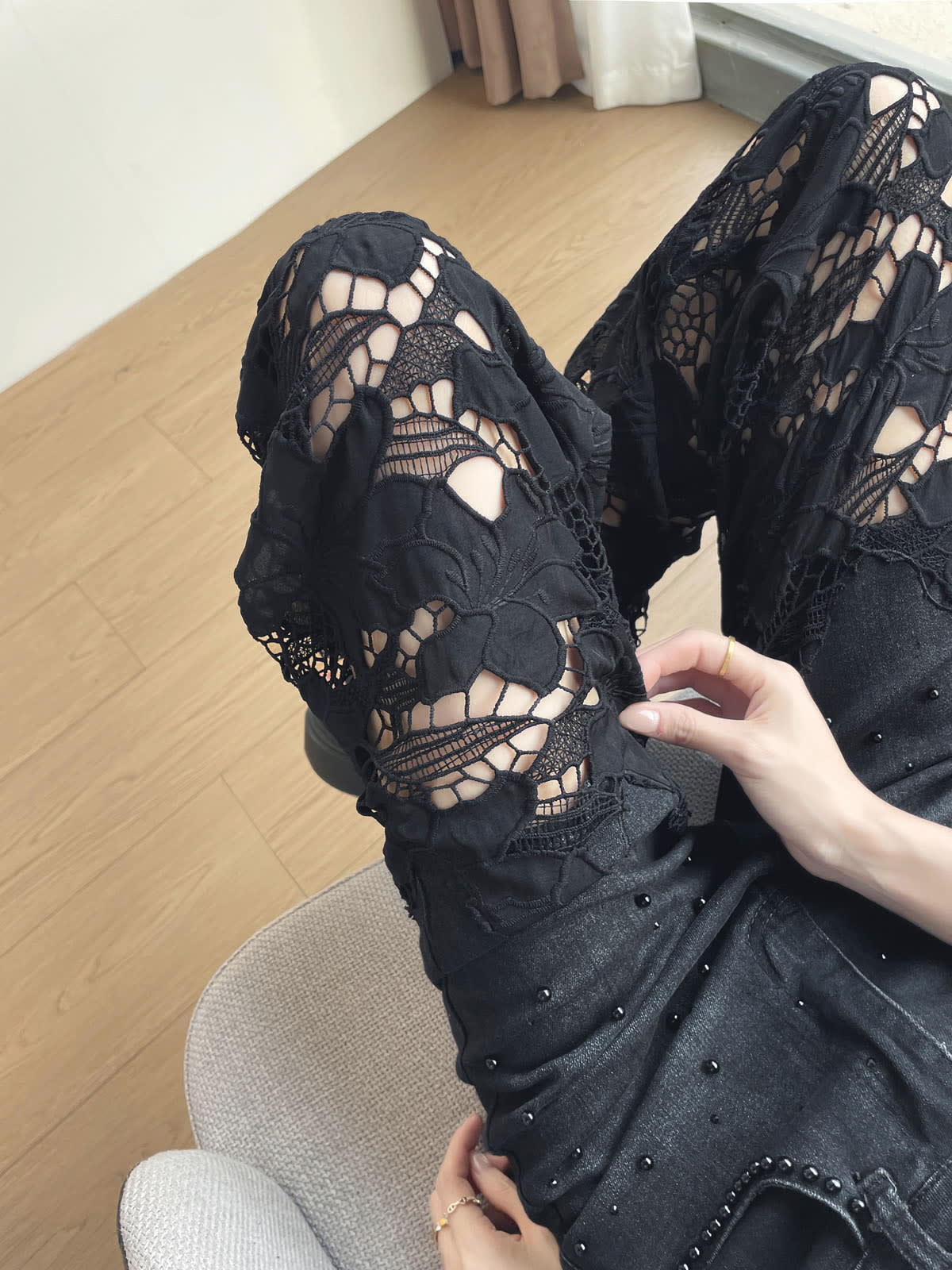 YEEYEEWang Wide-Leg Jeans in Solid Black, Asian-fit cut, waist-down view seated with knee bent up, hand touching the floral lace cutout panel on the leg.