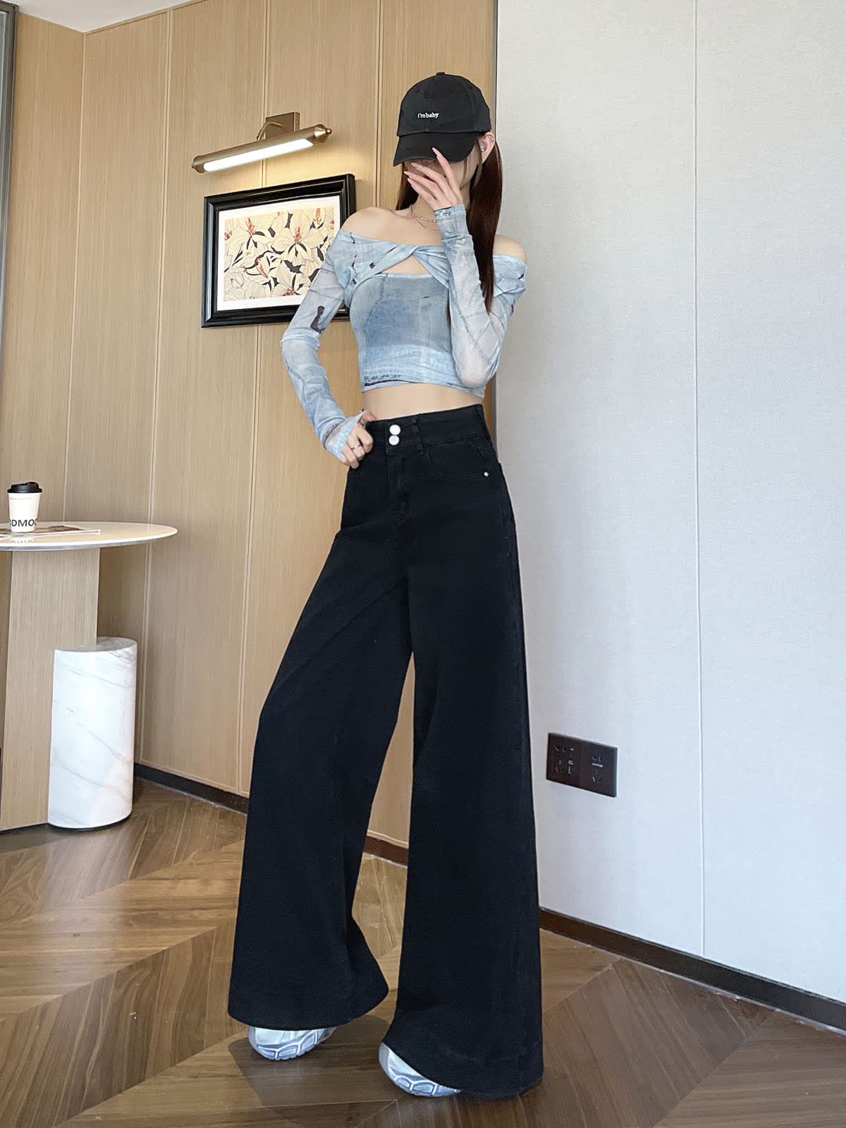 YEEYEEWang wide-leg jeans in Solid Black, Asian-fit cut, full-body standing pose in black cap, hand touching face, wood-paneled wall backdrop.
