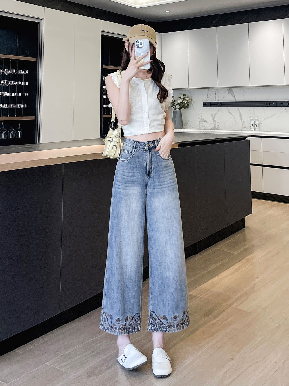 YEEYEEWang Wide-Leg Jeans in Light Blue, Asian-fit cut, full-body standing pose holding phone at face, beige cap and shoulder bag, paisley-embroidered hems.