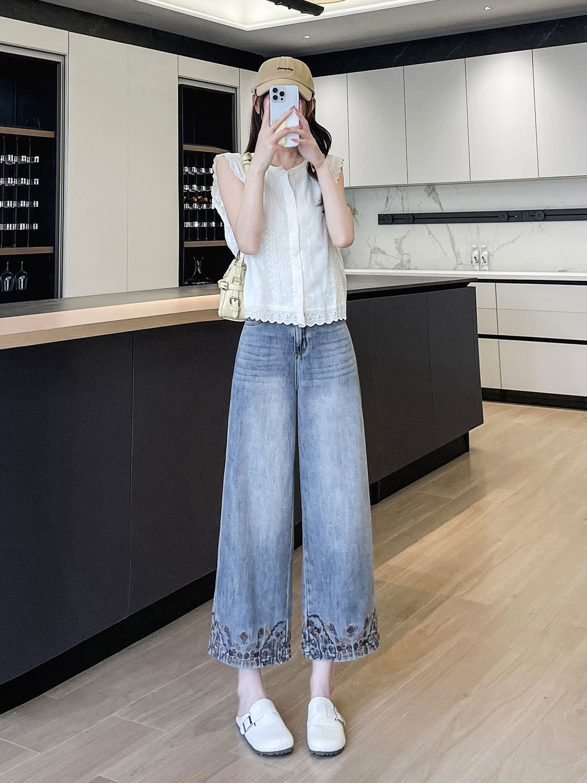 YEEYEEWang Wide-Leg Jeans in Light Blue, Asian-fit cut, full-body standing pose holding phone at face, white eyelet top and cream shoulder bag, embroidered hems in bright kitchen.