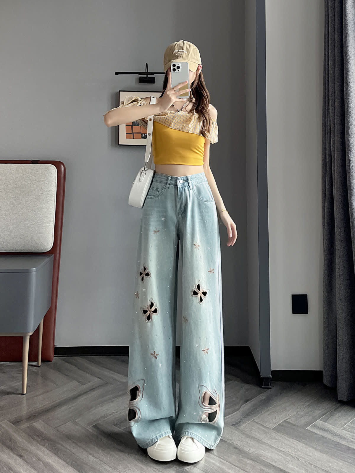 YEEYEEWang Wide-Leg Jeans in Light Blue, Asian-fit cut, full-body front pose holding phone at face, yellow off-shoulder top with beige cap and white shoulder bag, butterfly cutout embroidery, floor-sweeping drape.