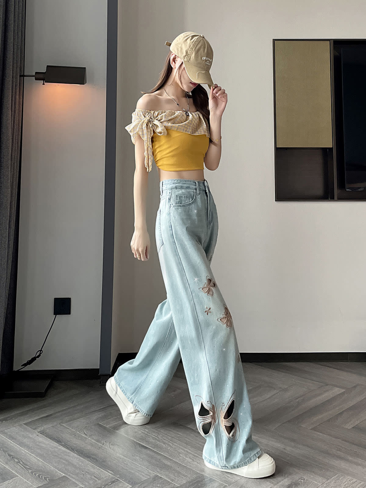 YEEYEEWang Wide-Leg Jeans in Light Blue, Asian-fit cut, full-body side walking pose touching cap brim, back patch pocket visible, butterfly cutout embroidery near the hem, floor-sweeping drape over white sneakers.