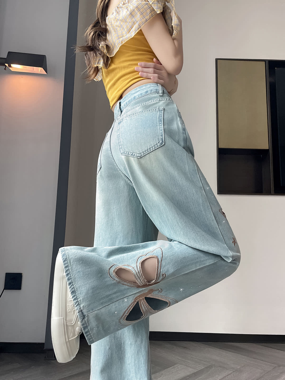 YEEYEEWang Wide-Leg Jeans in Light Blue, Asian-fit cut, waist-down side leg-kick pose, large butterfly cutout embroidery sweeping across the wide leg, scattered star stitching, white chunky sneakers.