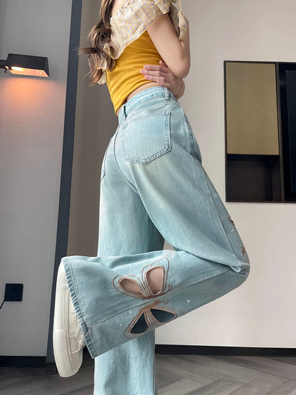 YEEYEEWang Wide-Leg Jeans in Light Blue, Asian-fit cut, waist-down side leg-kick pose, large butterfly cutout embroidery sweeping across the wide leg, scattered star stitching, white chunky sneakers.