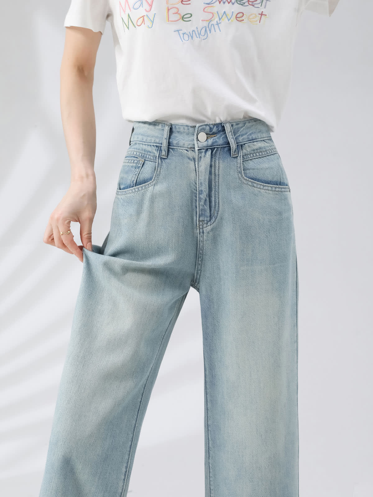 YEEYEEWang Wide-Leg Jeans in Light Blue, Asian-fit cut, waist-down front view, hand pulling leg fabric to show soft stretch drape, white graphic tee and metal button.