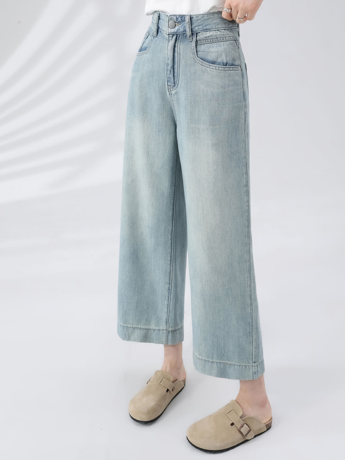 YEEYEEWang Wide-Leg Jeans in Light Blue, Asian-fit cut, waist-down front view, hand resting near metal button waistband with rings, wide stitched hems and beige clogs.