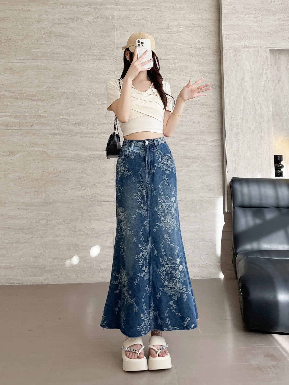 YEEYEEWang Jupe longue en jean Bleu, coupe Asian-fit, vue de face corps entier, debout avec téléphone devant le visage, autre main levée, casquette beige et sac noir, imprimé floral.