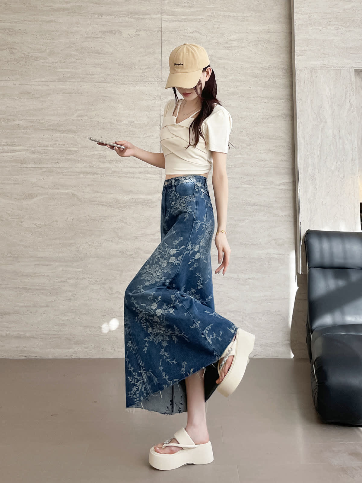 YEEYEEWang Jupe longue en jean Bleu, coupe Asian-fit, vue de côté corps entier, en marchant avec téléphone à la main, casquette beige, denim à imprimé floral au drapé fluide fendu.