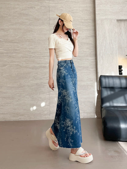 YEEYEEWang Jupe longue en jean Bleu, coupe Asian-fit, vue de côté corps entier, debout avec main touchant la visière de la casquette, denim à imprimé floral au drapé balayant le sol, ourlet brut.
