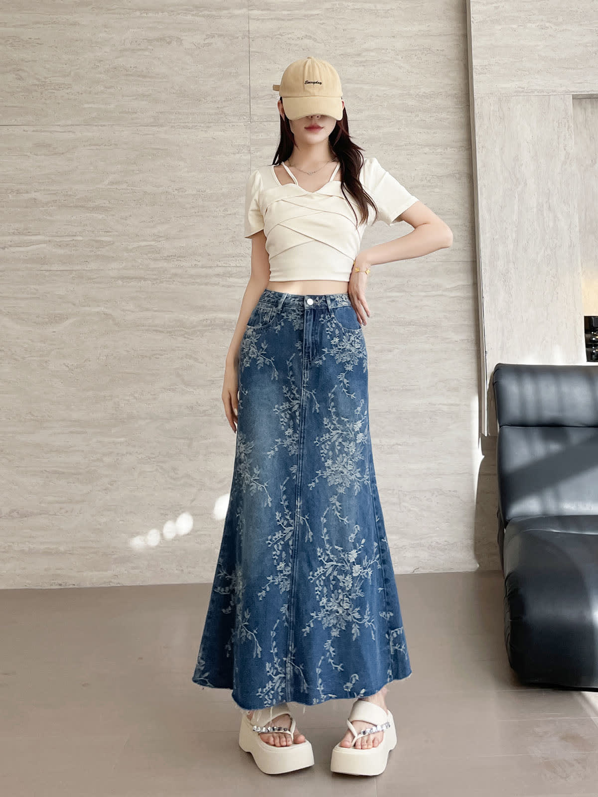 YEEYEEWang Jupe longue en jean Bleu, coupe Asian-fit, vue de face corps entier, debout main sur la hanche, casquette beige, denim à imprimé floral boutonné au drapé évasé balayant le sol.