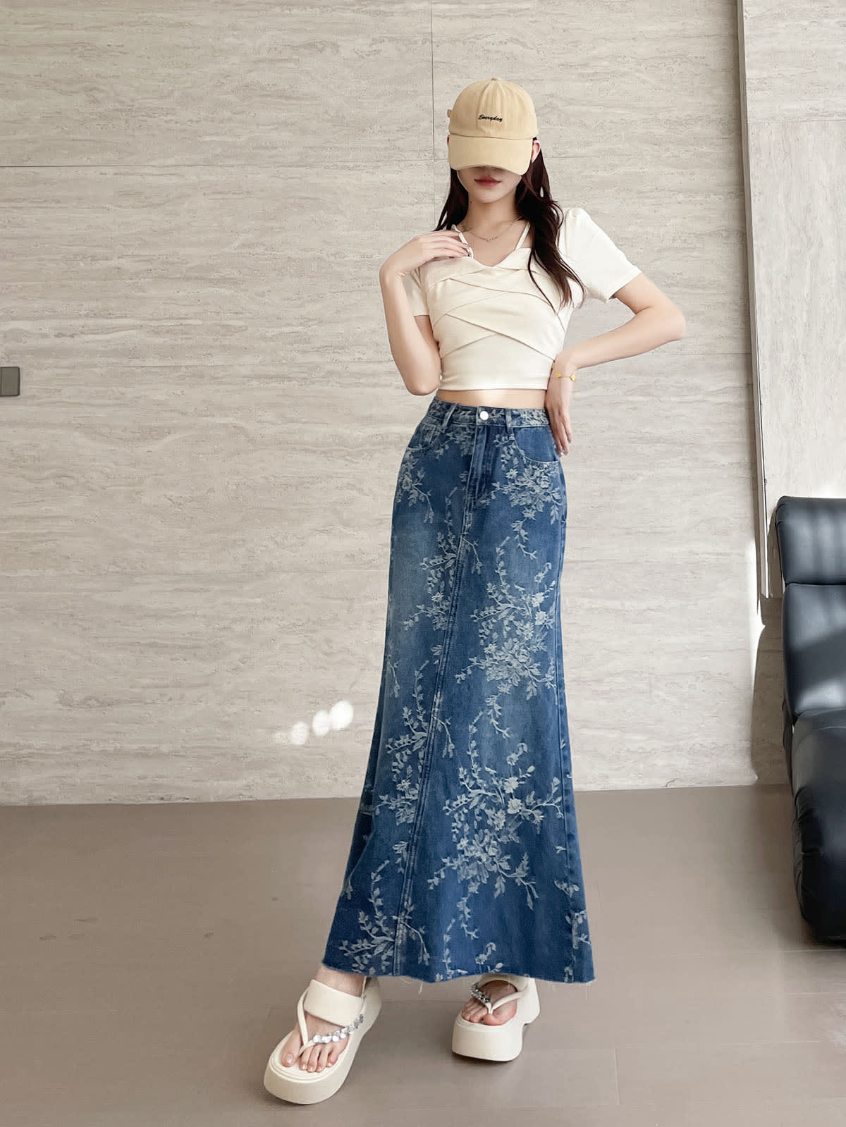 YEEYEEWang Jupe longue en jean Bleu, coupe Asian-fit, vue frontale pied-à-terre debout, une main au col et une sur la hanche, jean jacquard floral, casquette beige.