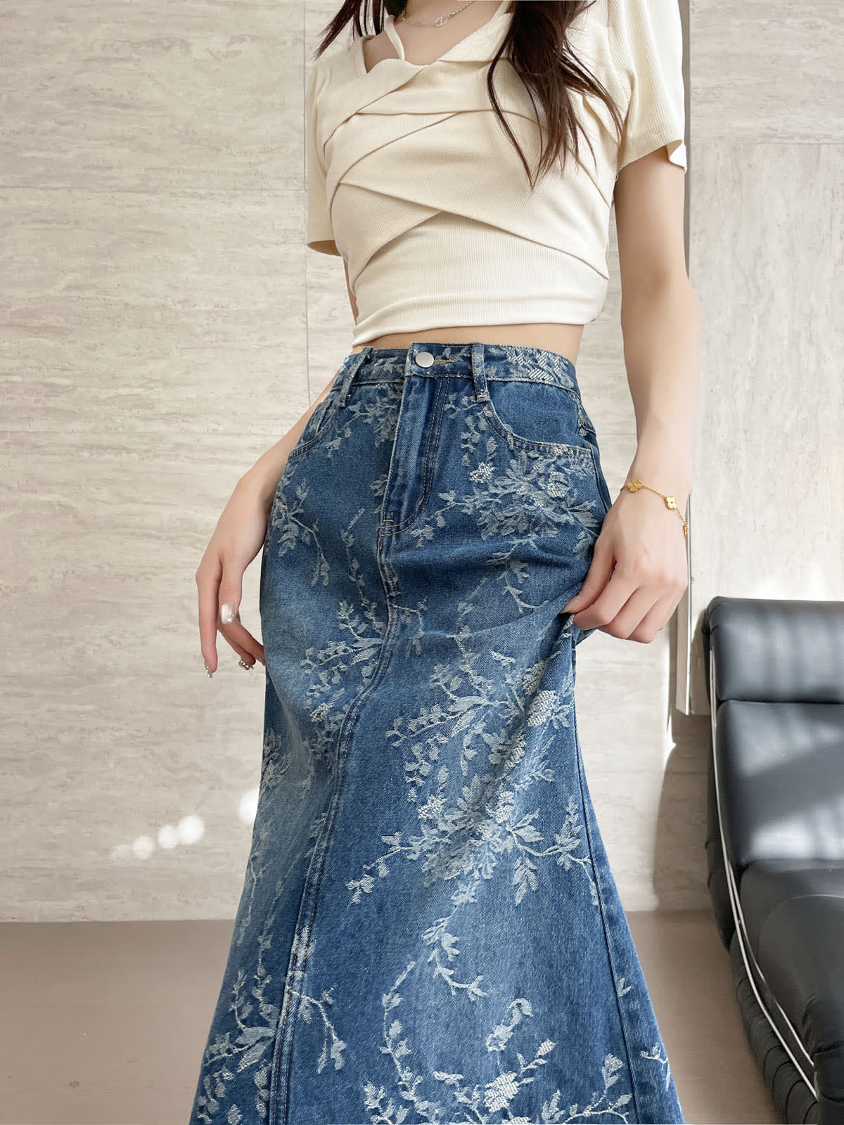 YEEYEEWang Jupe longue en jean Bleu, coupe Asian-fit, vue frontale mi-corps, une main soulevant le côté de la jupe, poches avant et bouton métal sur jean jacquard floral.