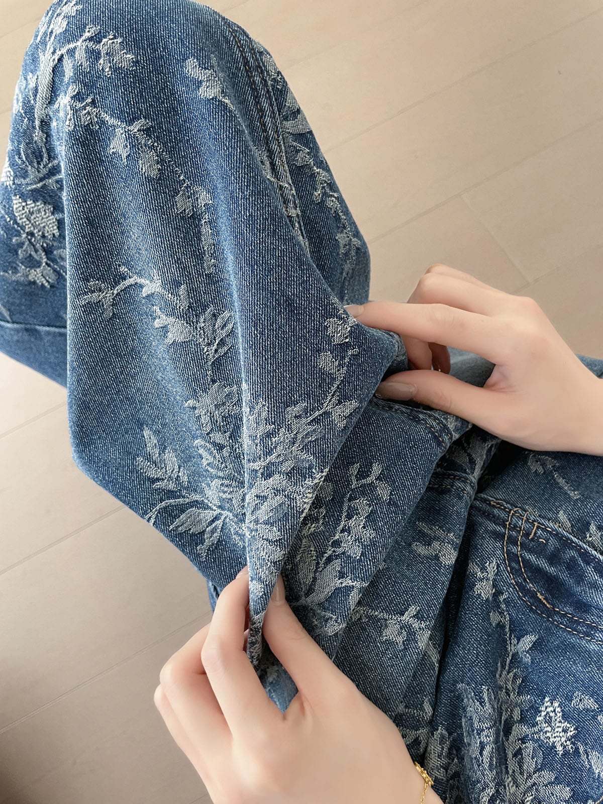 YEEYEEWang Jupe longue en jean Bleu, coupe Asian-fit, gros plan sur la texture du jean jacquard floral, mains soulevant le bord du tissu.