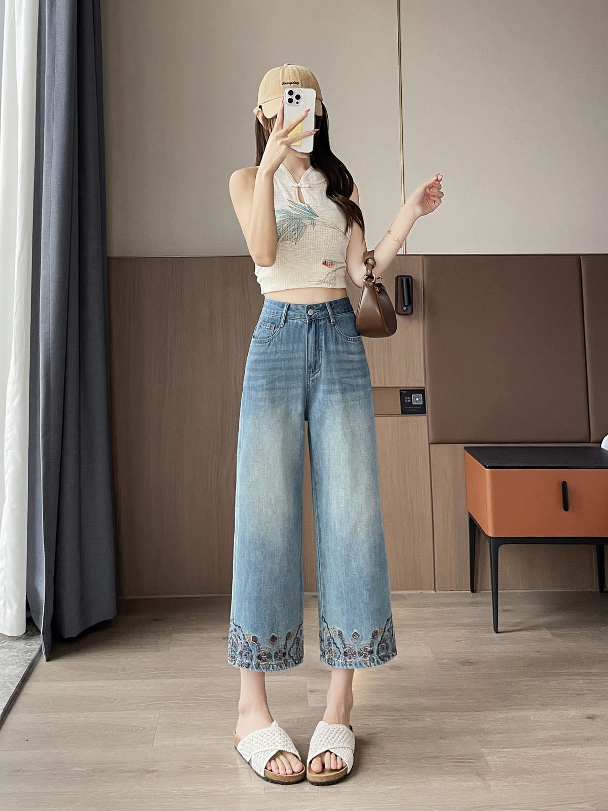 YEEYEEWang Straight Jeans in Vintage Blue, Asian-fit cut, full-body front standing pose holding phone at face, cap and brown shoulder bag, floral-embroidered hems.