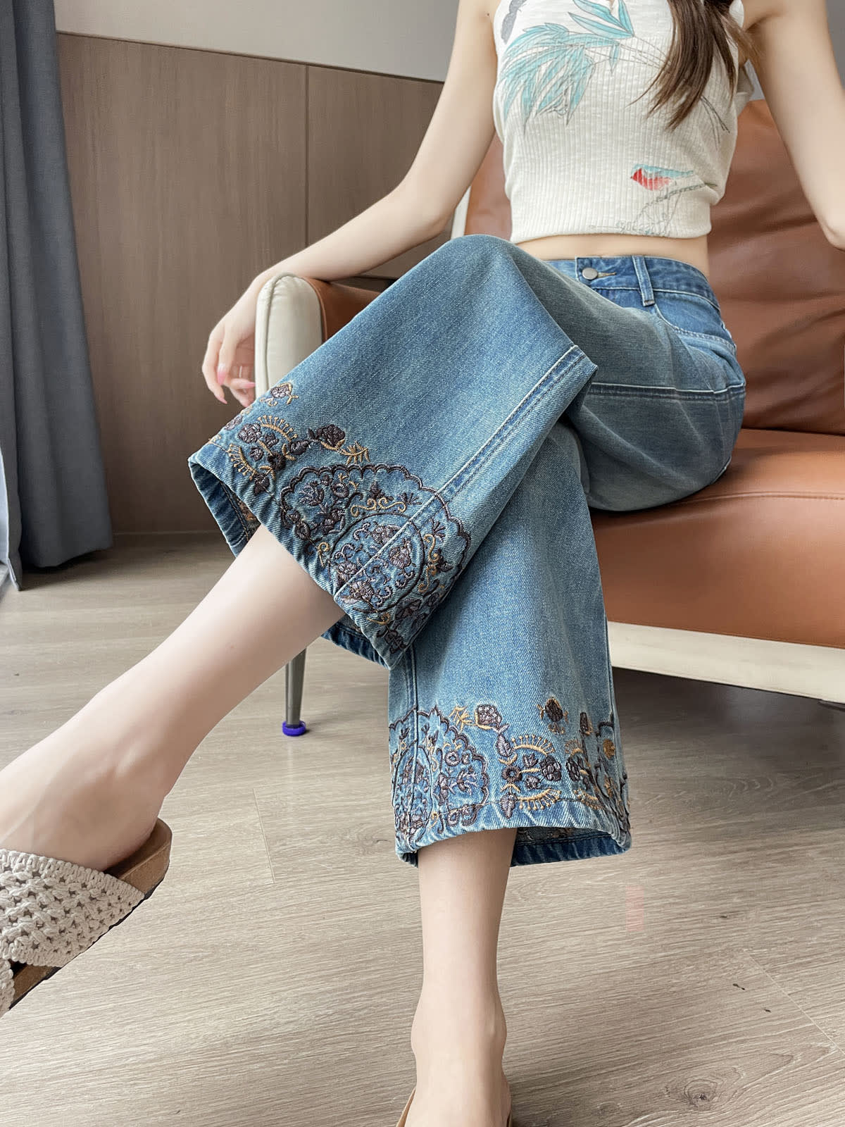 YEEYEEWang Straight Jeans in Vintage Blue, Asian-fit cut, waist-down seated pose with legs crossed, embroidered floral hems in close view.