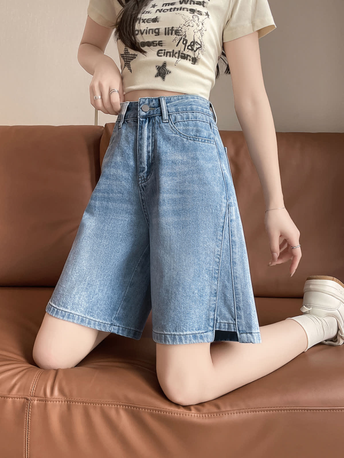 YEEYEEWang Denim Bermuda Shorts in Blue, Asian-fit cut, waist-down front view kneeling on a leather sofa, showing the relaxed wide-leg drape.