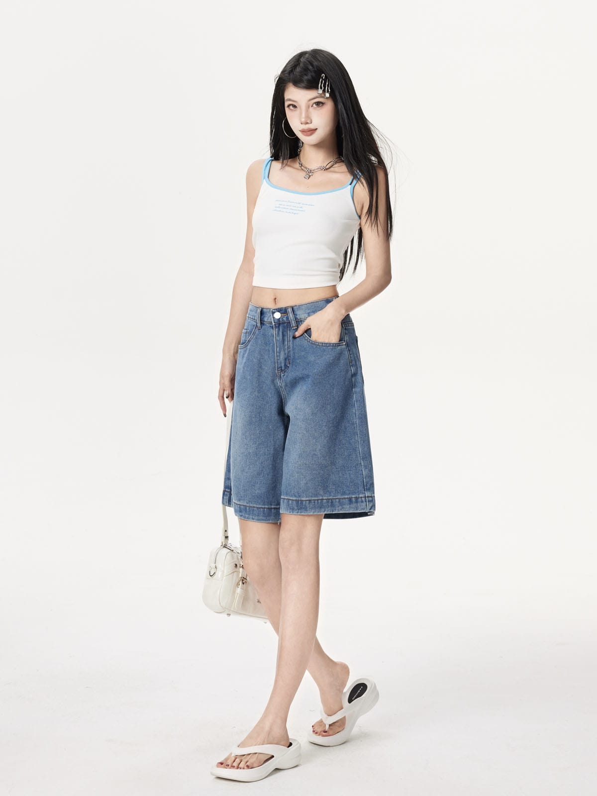 YEEYEEWang Denim Bermuda Shorts in Blue, Asian-fit cut, full-body three-quarter standing pose holding a white handbag at side, one hand in front pocket.