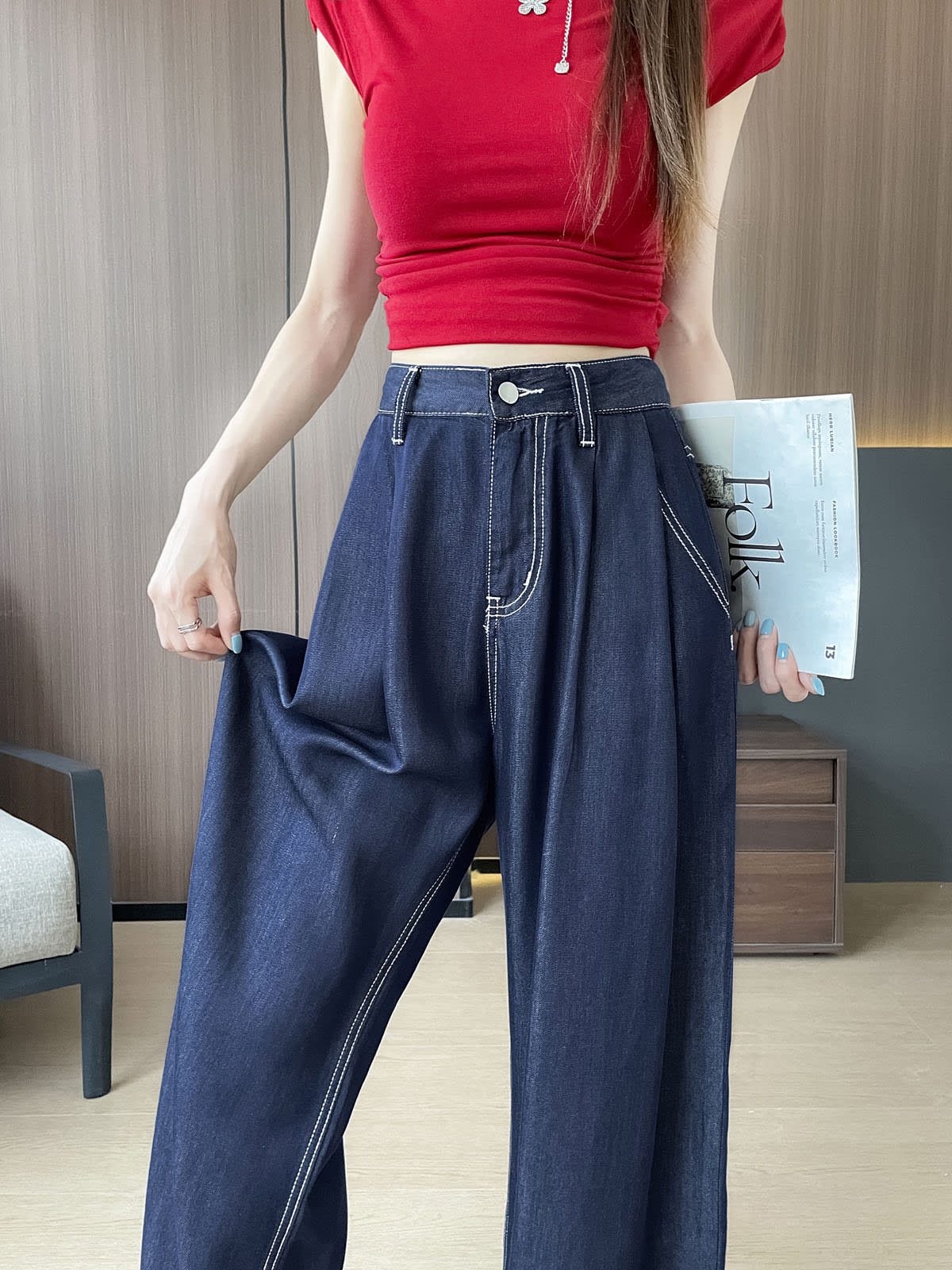 YEEYEEWang Wide-Leg Jeans in Denim Blue, Asian-fit cut, waist-down front view, one hand pinching the flowing fabric to show drape, the other holding a magazine.
