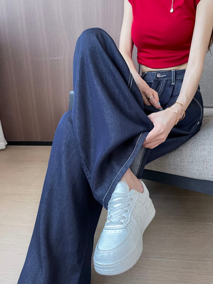 YEEYEEWang Wide-Leg Jeans in Denim Blue, Asian-fit cut, waist-down seated pose on sofa, one hand lifting the hem, paired with white sneakers.