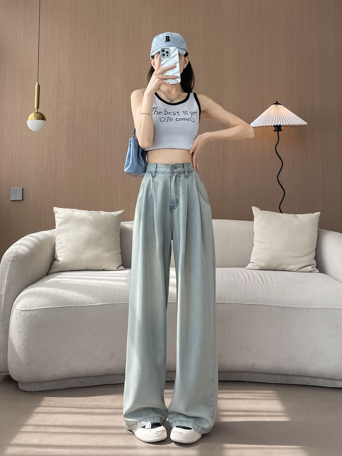 YEEYEEWang Wide-Leg Jeans in Light Blue, Asian-fit cut, full-body front pose holding phone at face, styled with cap, tank top and blue shoulder bag.