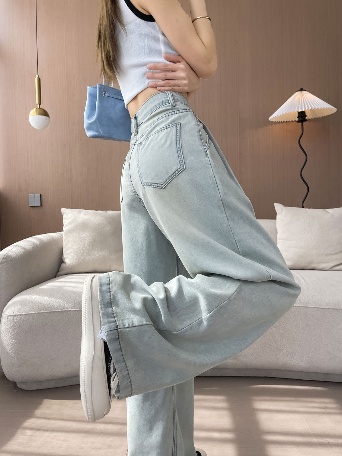 YEEYEEWang Wide-Leg Jeans in Light Blue, Asian-fit cut, waist-down side view with leg-kick pose showing back patch pocket and fluid drape, blue bag on shoulder.